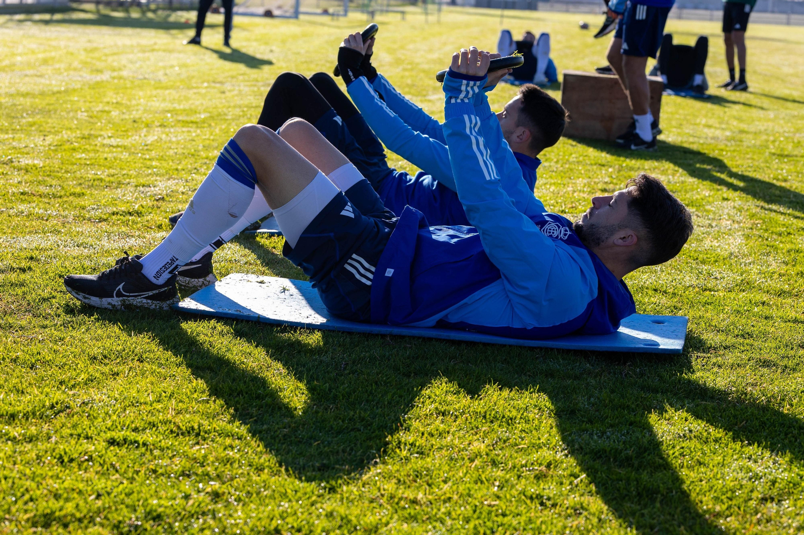Varios jugadores realizan ejercicios de fuerza en el césped de la Ciudad Deportiva