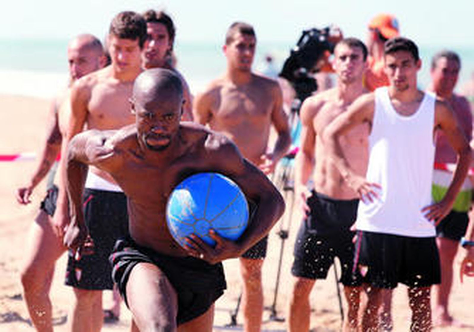 Zokora se ejercita en la playa con un balón medicinal ante la mirada del resto de sus compañeros.