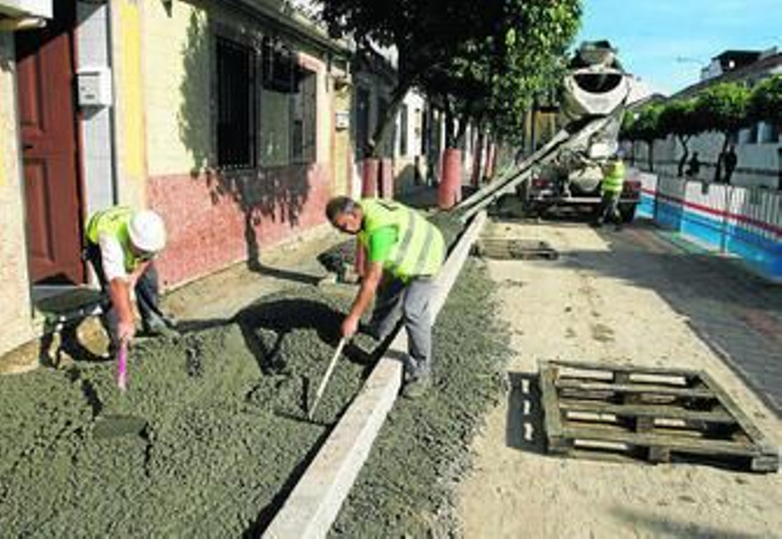 Dos obreros trabajan en uno de los acerados de la calle Ciudad de Carmona.