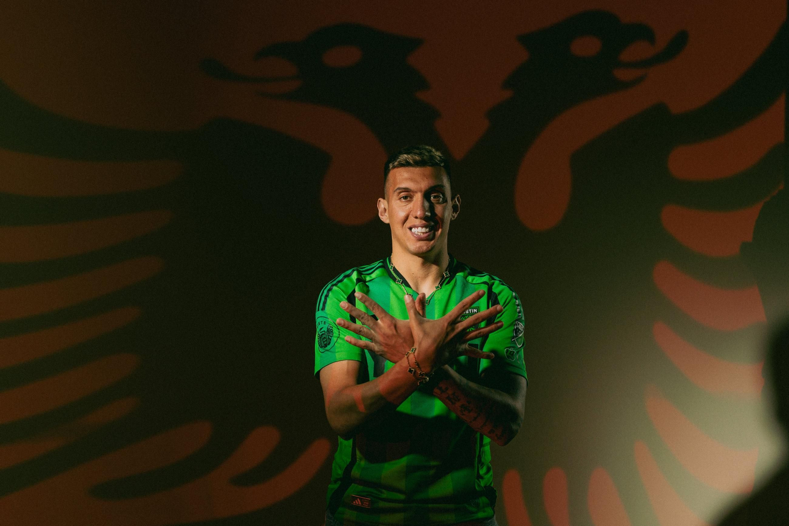 Uzuni, con la camiseta del Austin y la bandera de Albania detrás.