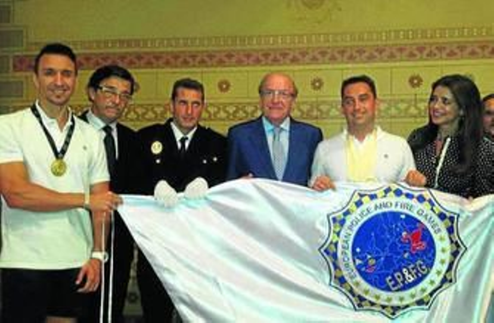 Pedro Rodríguez sostiene y participantes de los Juegos sostienen la bandera.