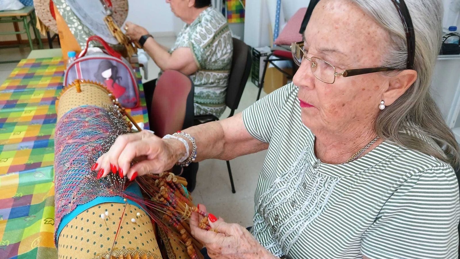 Dos alumnas haciendo varios diseños de encaje de bolillos.