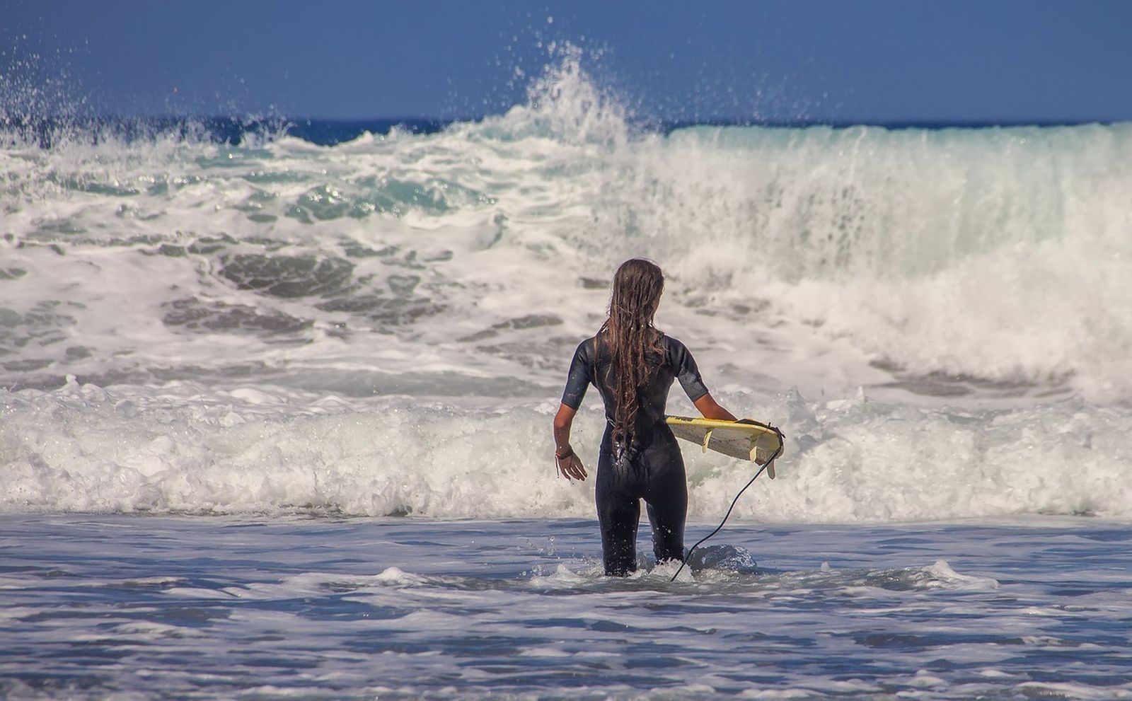 Mujer se adentra en el mar con la tabla de surf.