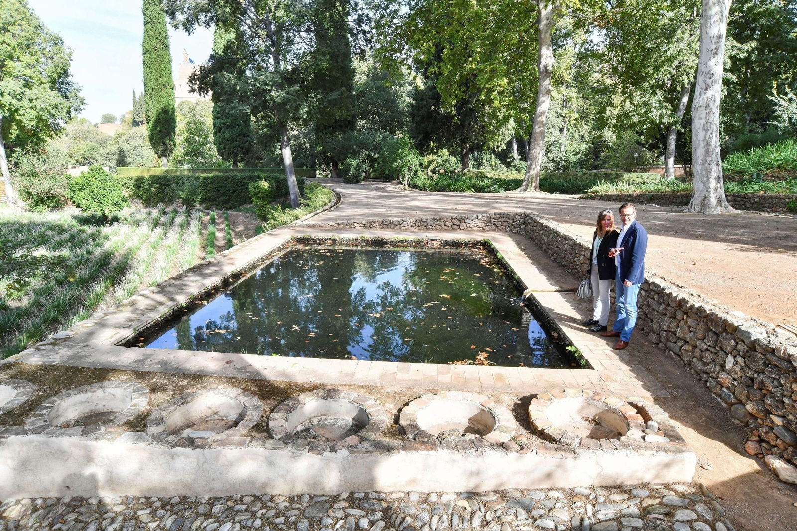 Una pareja pasea junto a la alberca de un municipio de Granada.
