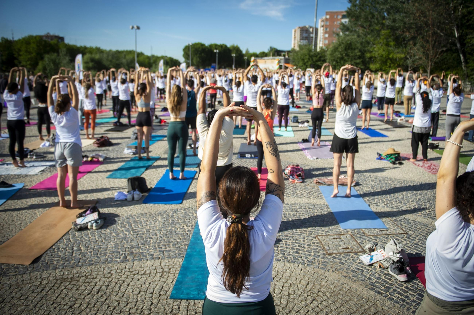 Un grupo de personas realiza ejercicios de estiramientos durante una sesión de yoga en una explanada en España.