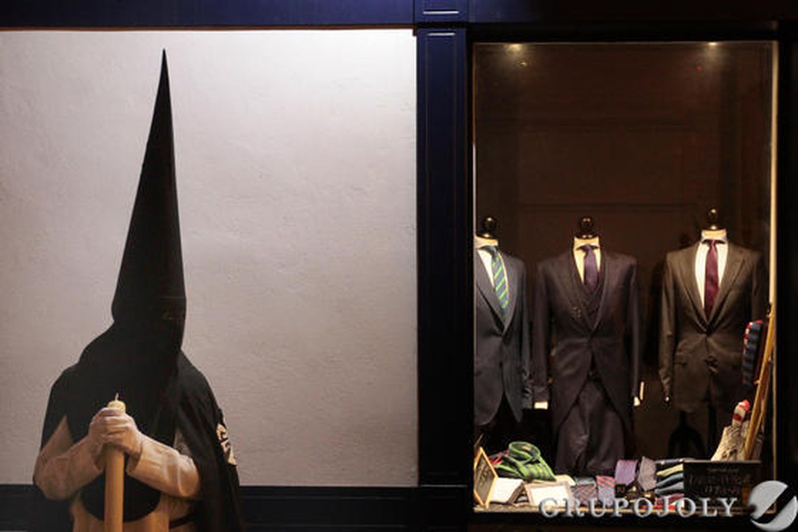 Un nazareno de la Hermandad de la Oración en el Huerto parado junto a un escaparate de la calle Bizcocheros donde se venden trajes de chaqueta.

Foto: Jose Contreras