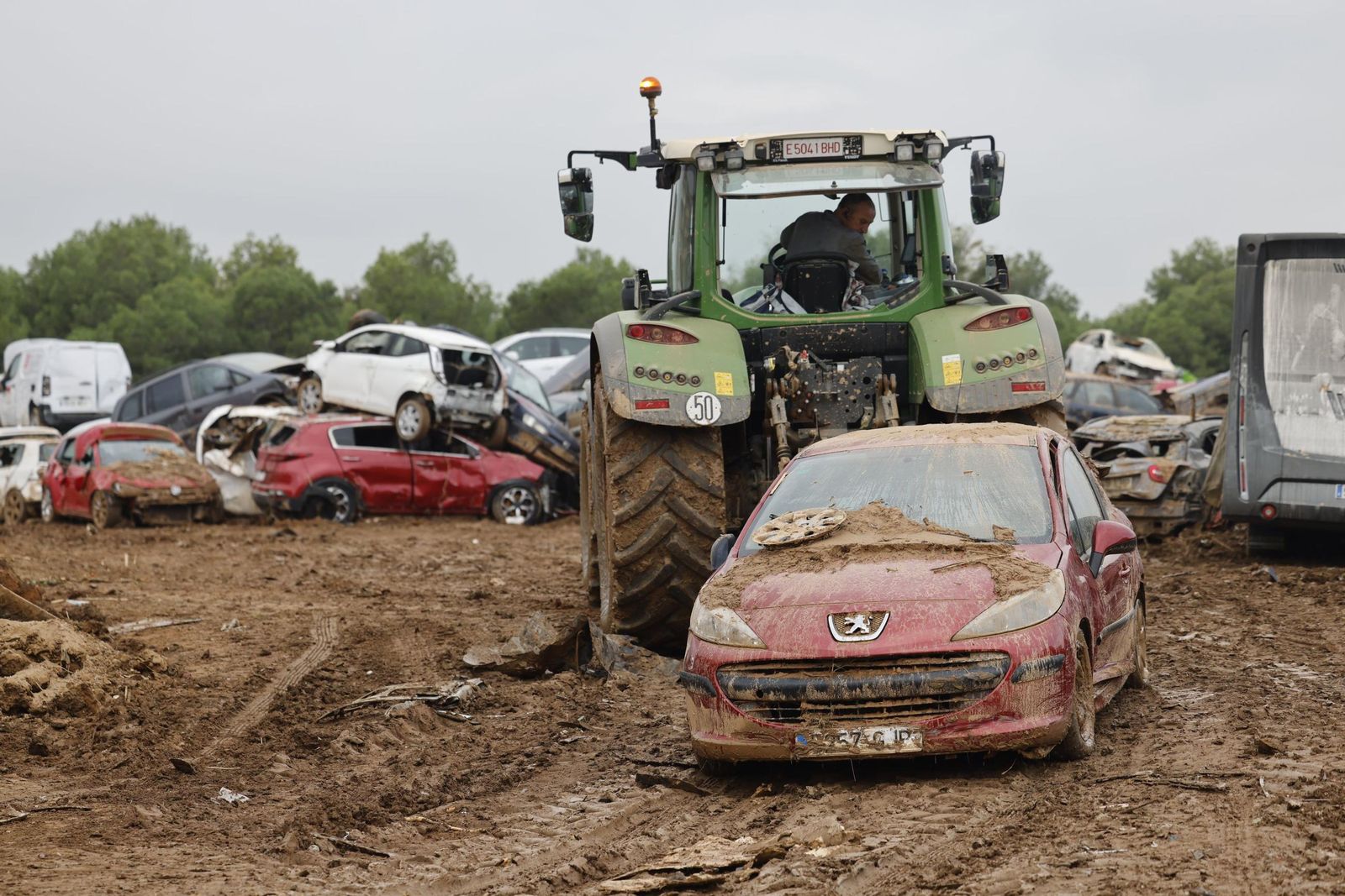 Un hombre traslada un coche destrozado por las riadas en el descampado habilitado en Paiporta.
