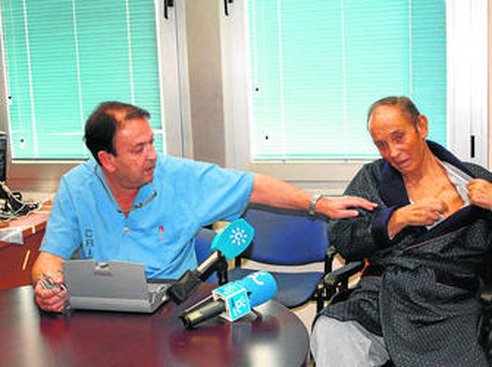 Jesús Burgos muestra el desfibrilador de Ángel Pérez (derecha) que se conecta al módem que hay sobre la mesa.