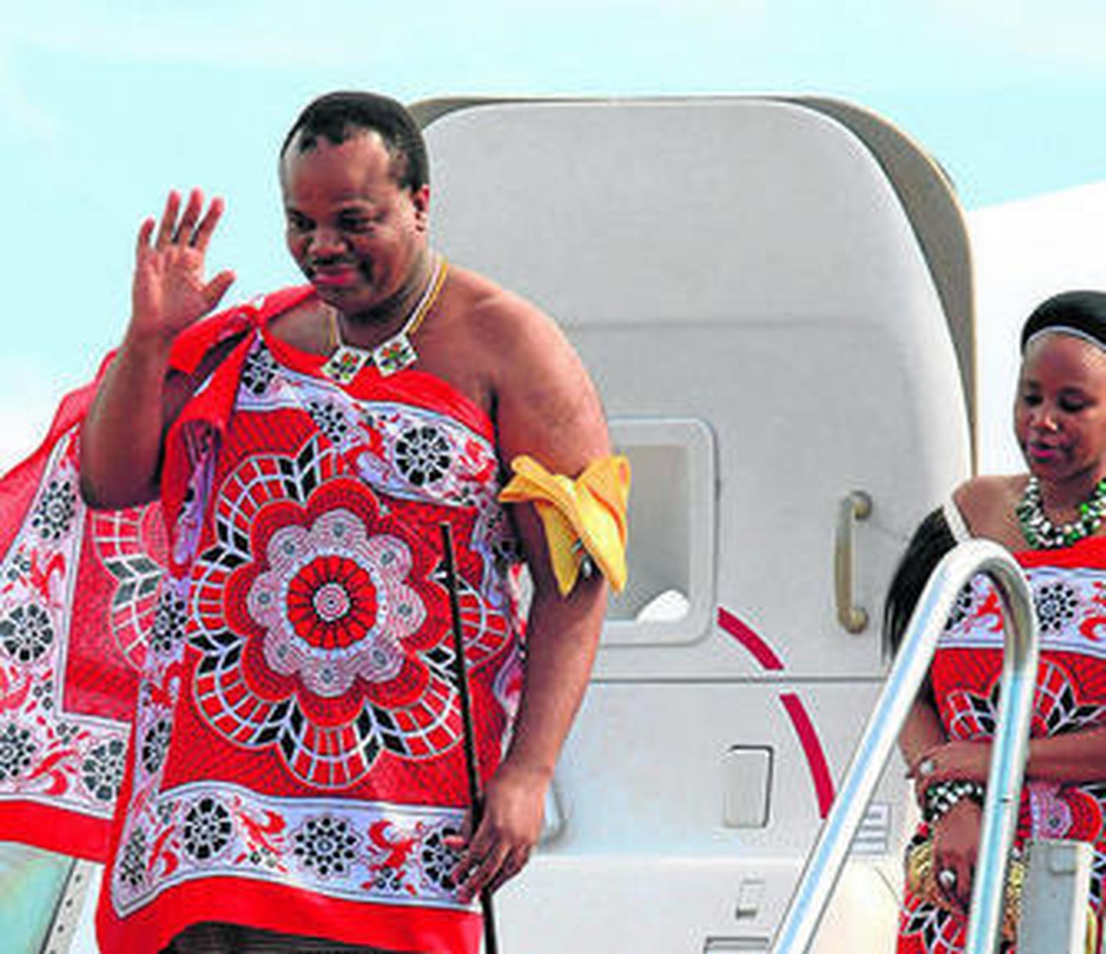 El rey bajando de su avión seguido por una de sus esposas.
