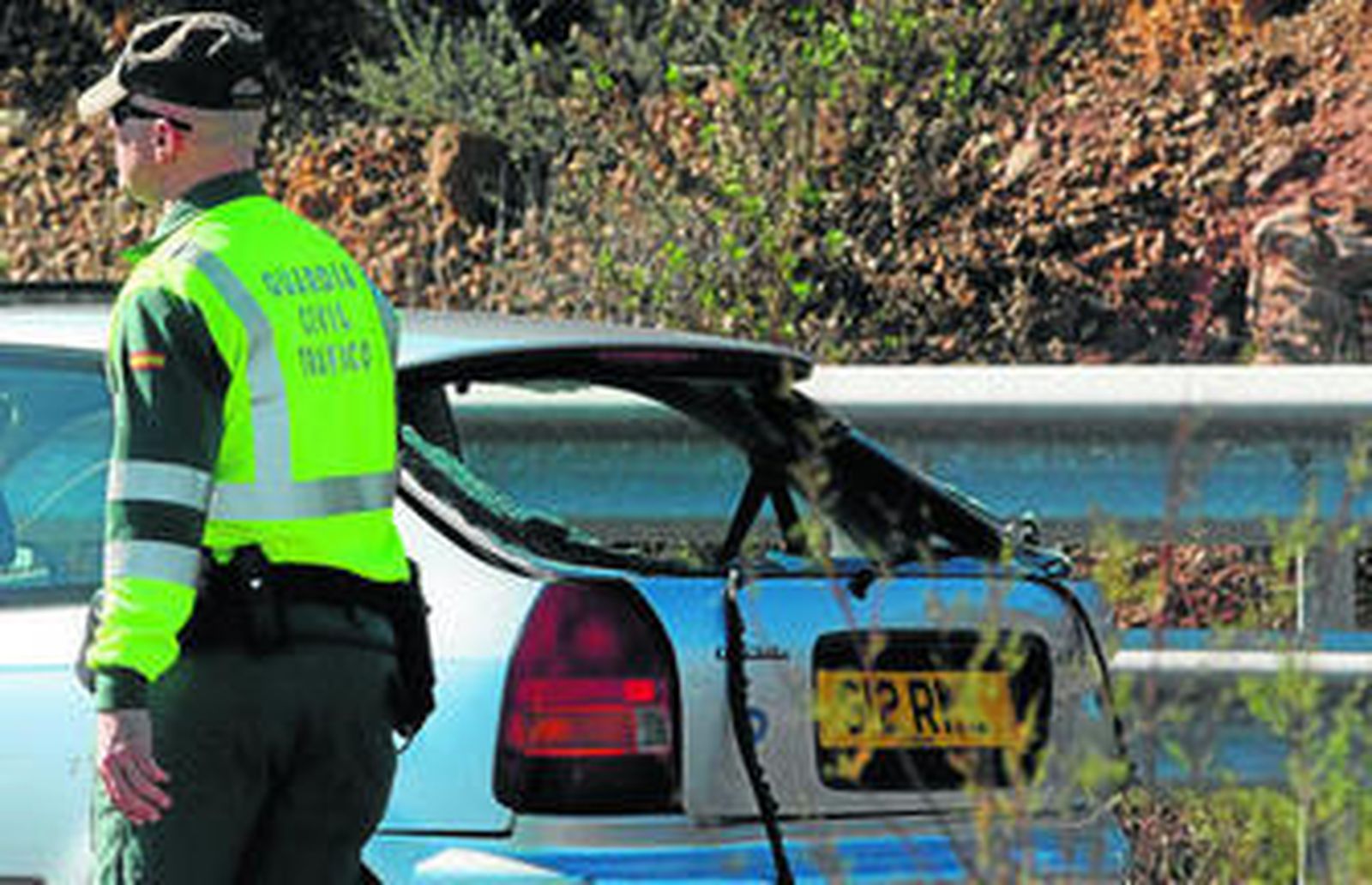 Detalle del turismo con la luna trasera rota junto a uno de los agentes de la Guardia Civikl de Tráfico que intervino tras el accidente.