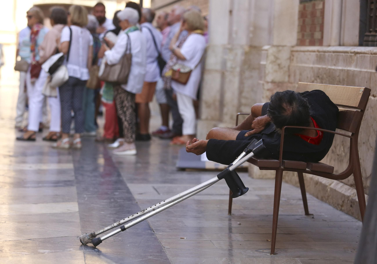 Un indigente duerme en un banco en una calle de Málaga.