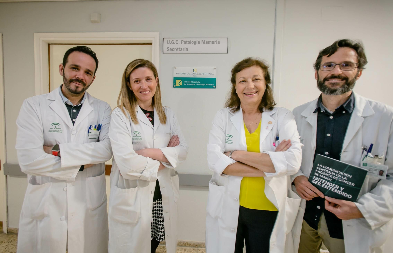 Alejandro Utor sostiene la guía junto al resto del equipo médico de la Unidad de Mama, delante de la placa con la acreditación de la SESPM.