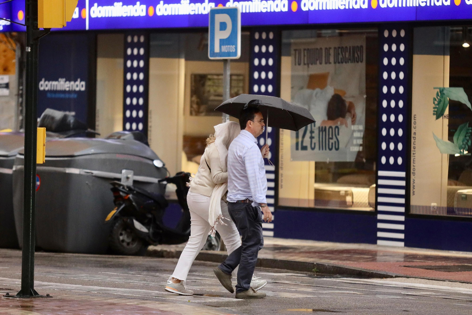 Una pareja se protege de la lluvia con un paraguas en una céntrica calle de Málaga Una pareja se protege de la lluvia con un paraguas en una céntrica calle de Málaga