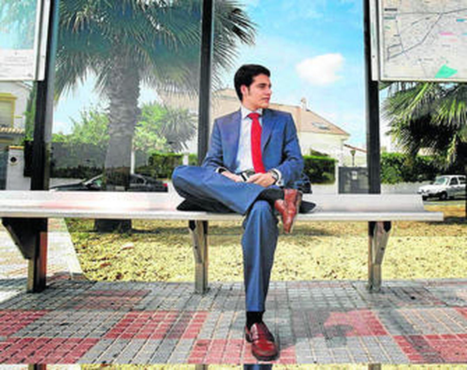 Un joven trajeado espera el autobús en una marquesina en una urbanización de chalés de Tomares.