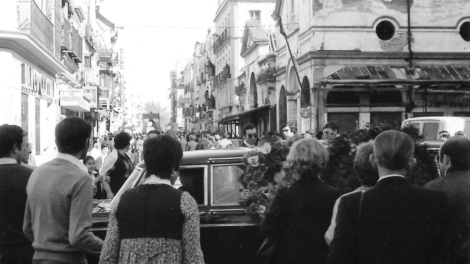 Contrastes de un Viernes Santo. El coche fúnebre en primer plano y la Esperanza, al fondo.