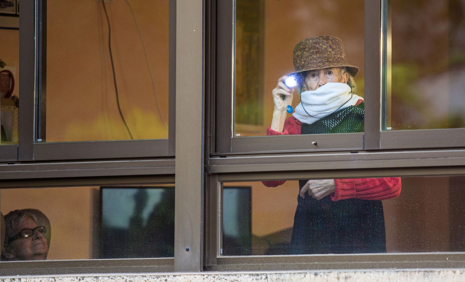 Una mujer mayor saluda desde su residencia con una lamparilla.
