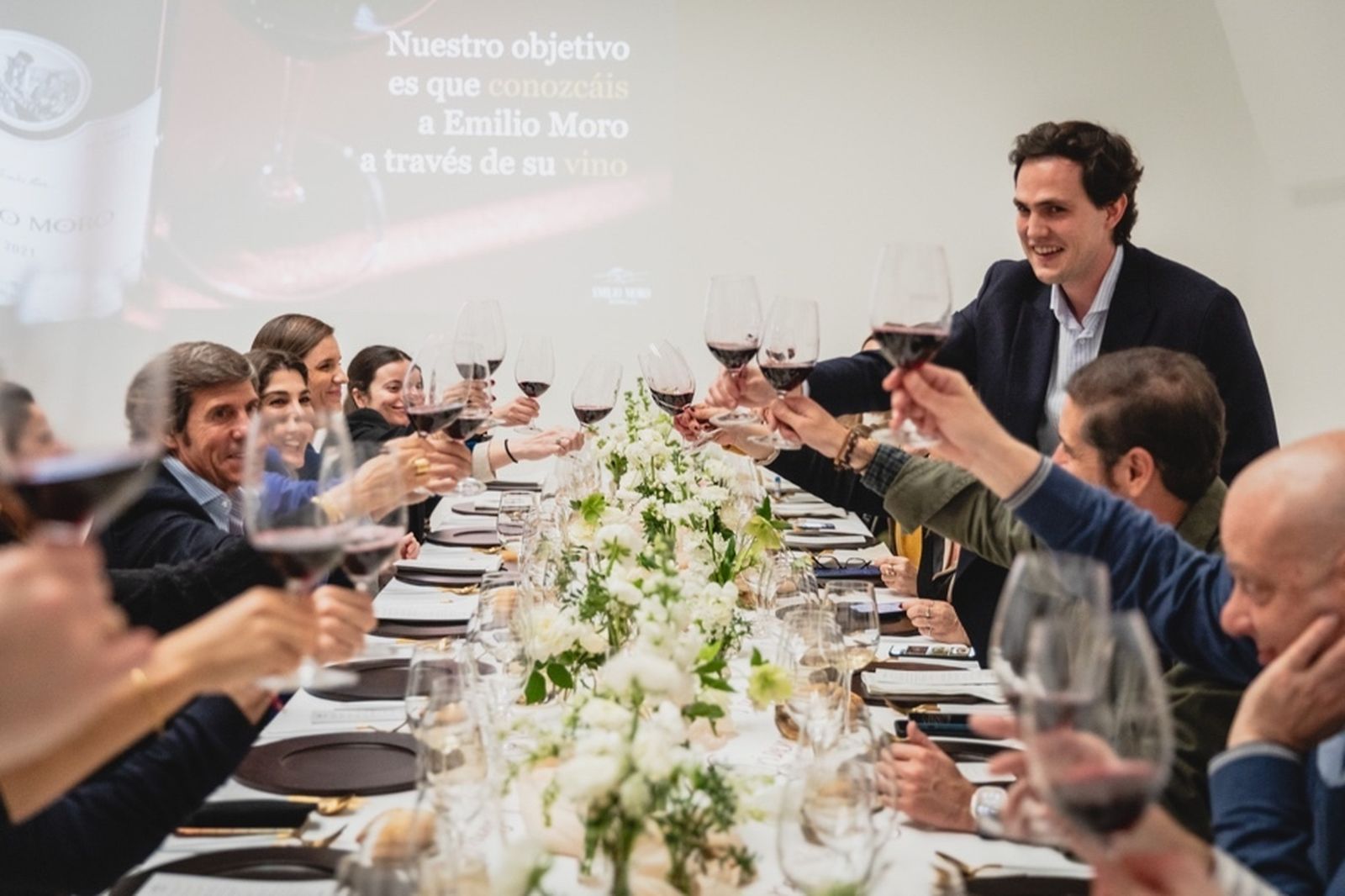 Javier Moro sentado brindando a la izquierda y Héctor Medina Moro de pie a la derecha rodeados de los invitados al evento.