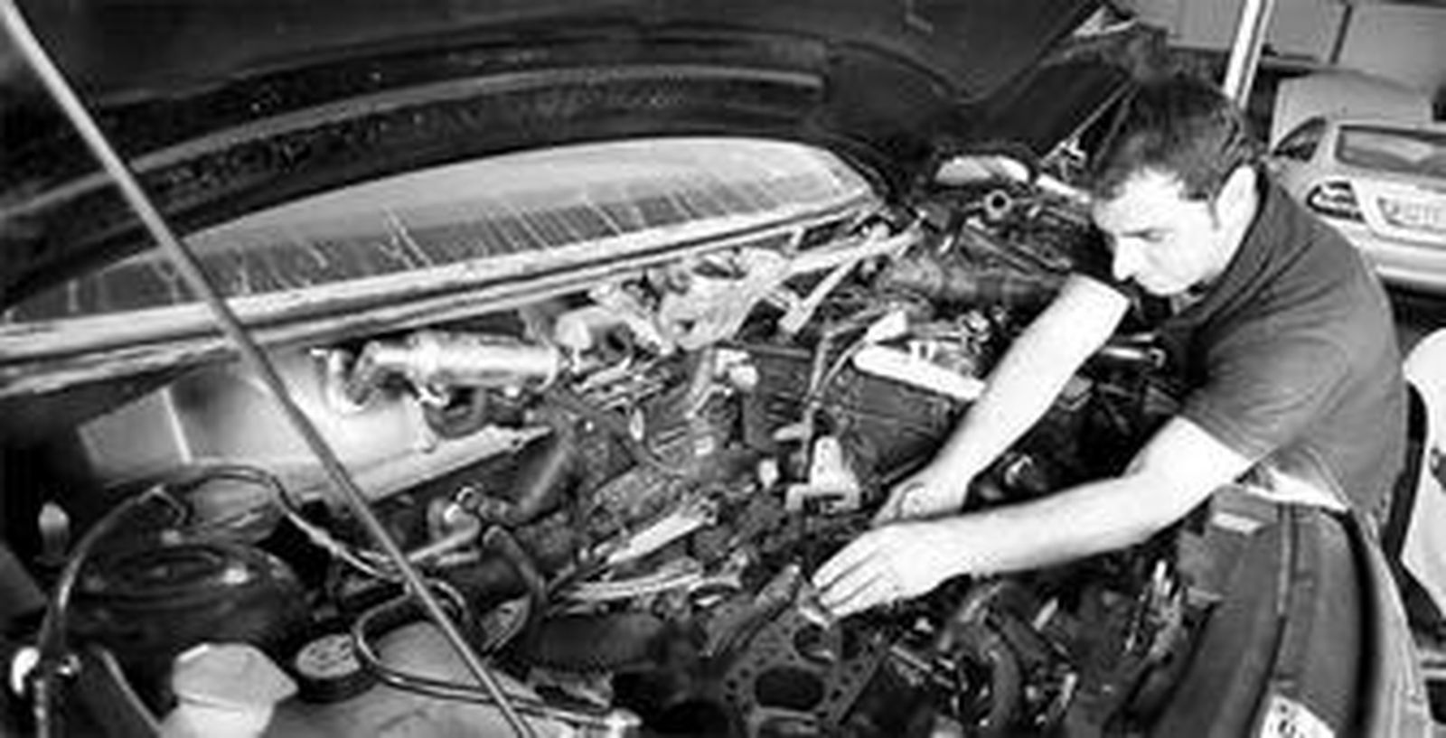 Un operario de un taller de reparación revisa el motor de un coche.