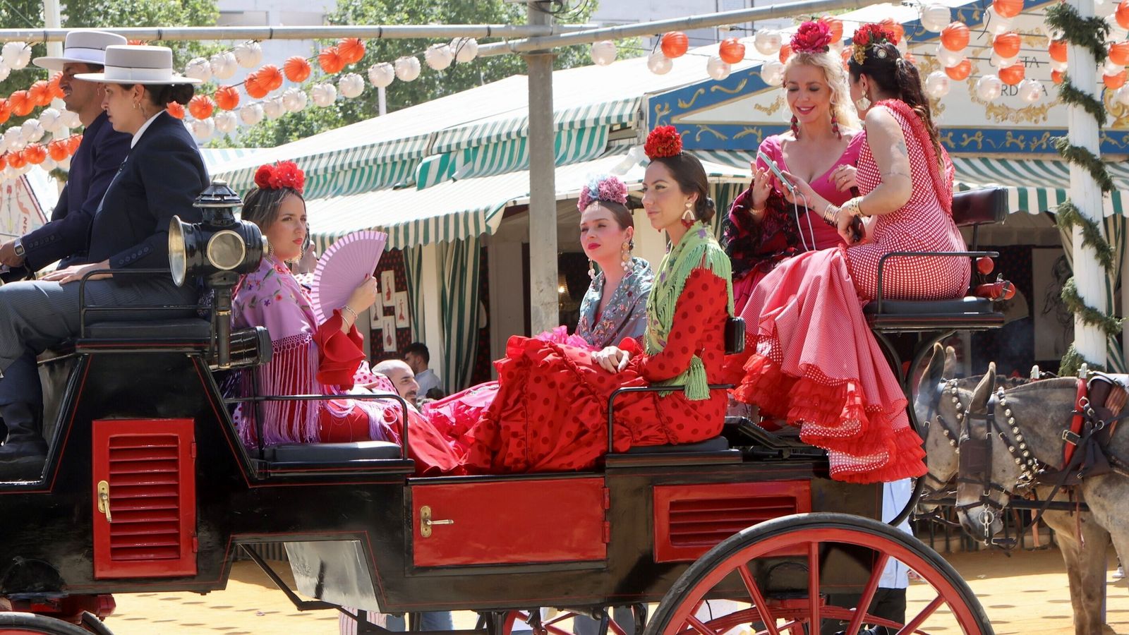 Varias flamencas se desplazan por el real en coche de caballos.