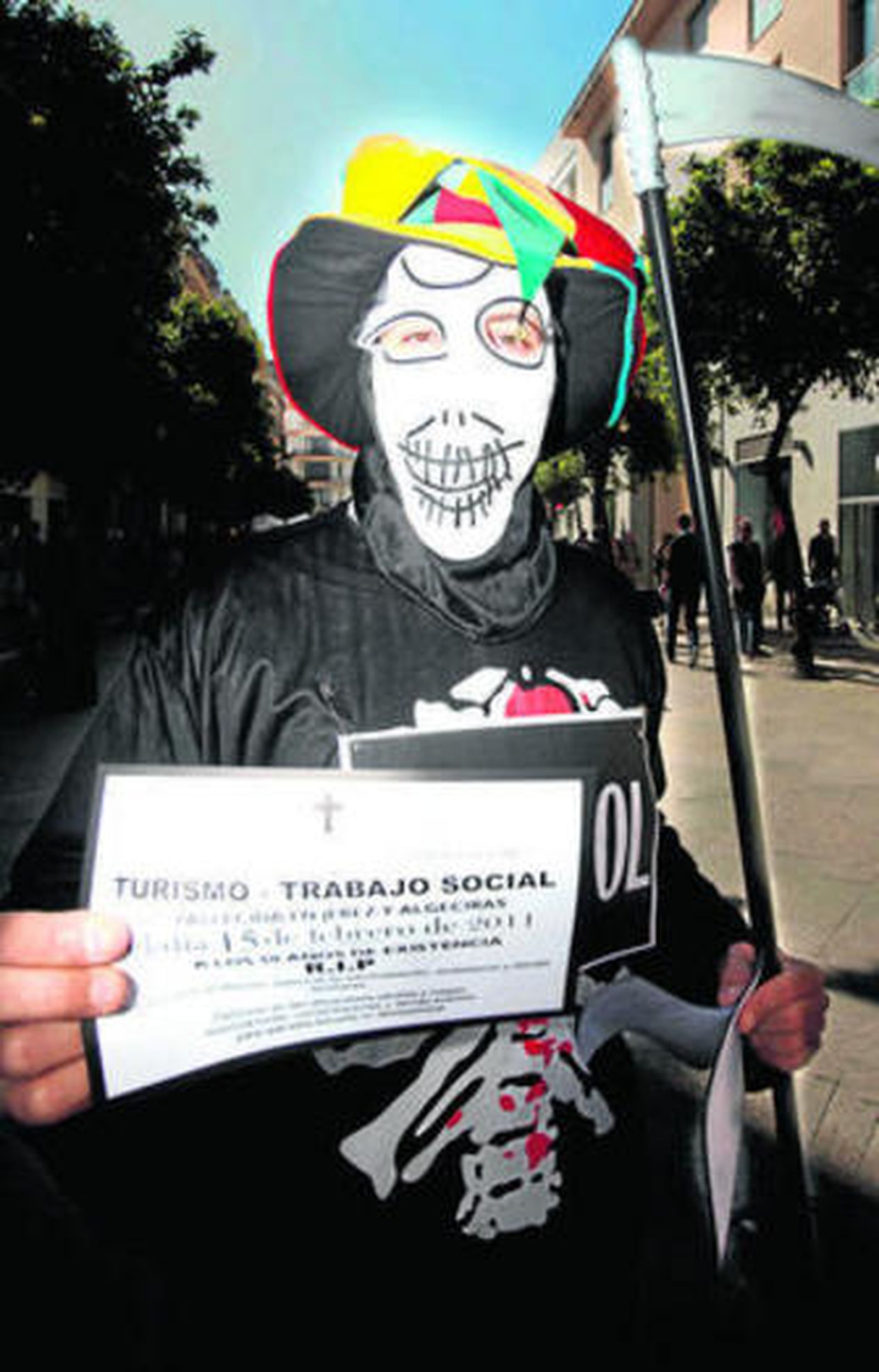 Un personaje disfrazado de la muerte muestra una esquela del centro.
