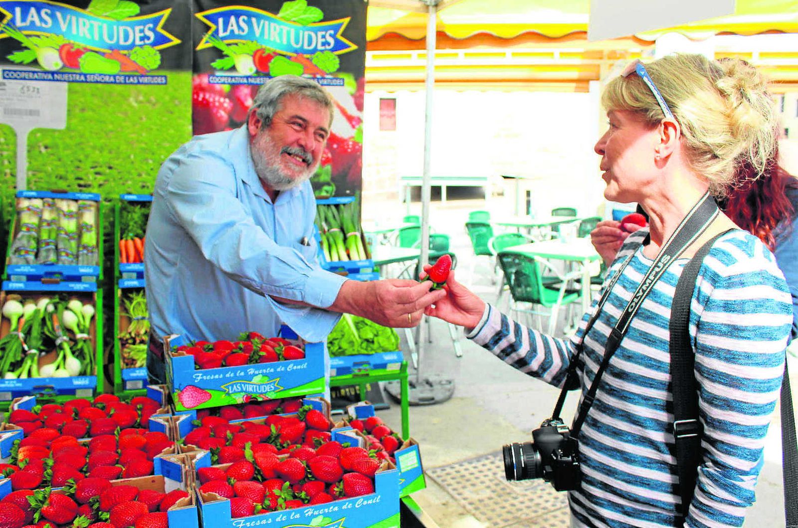Una turista recoge una fresa de manos de Bartolomé Ramírez, presidente de la Cooperativa Las Virtudes, de Conil.