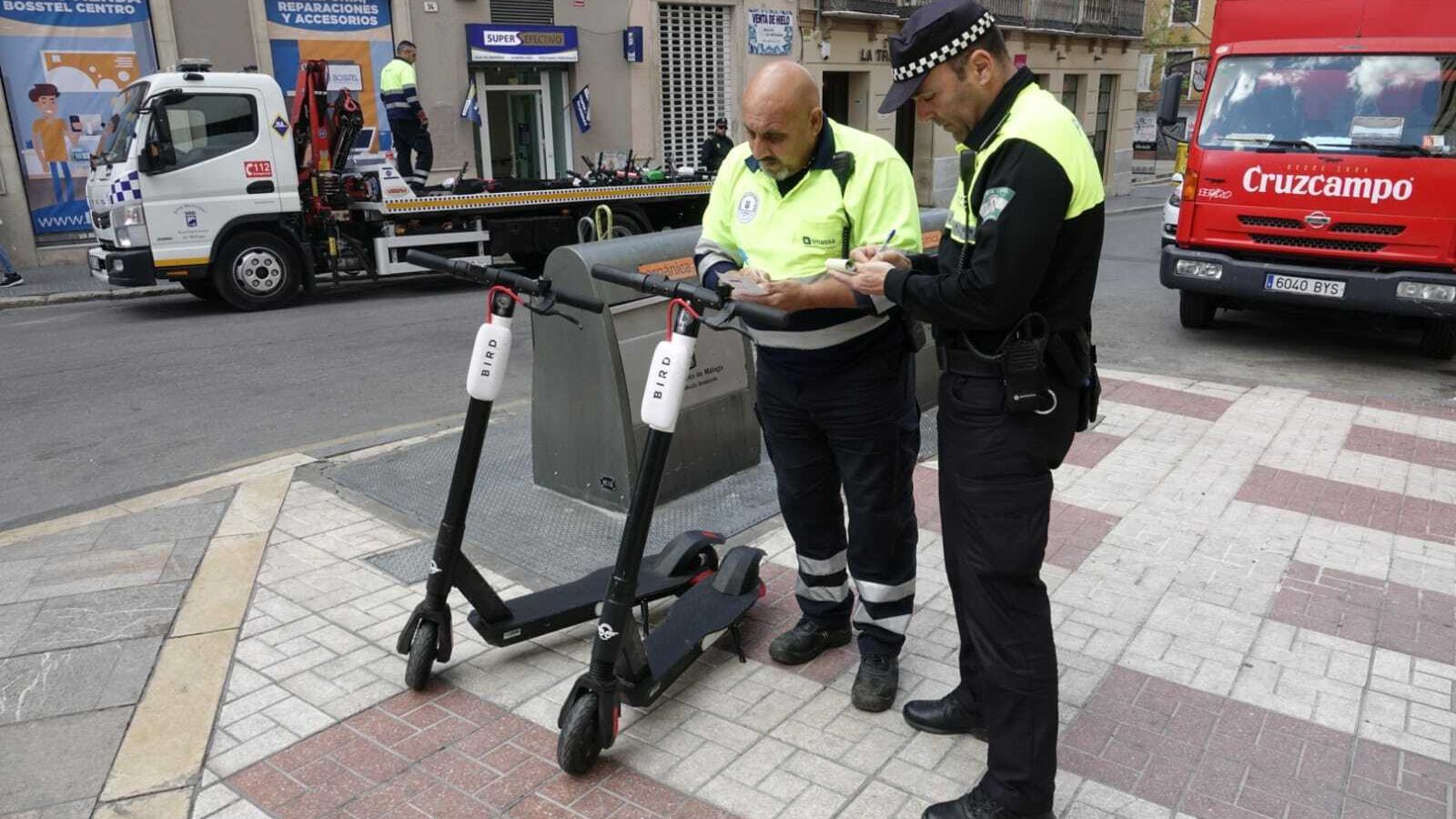Un agente de la Policía Local y un operario de la grúa proceden a multar y retirar dos patinetes.