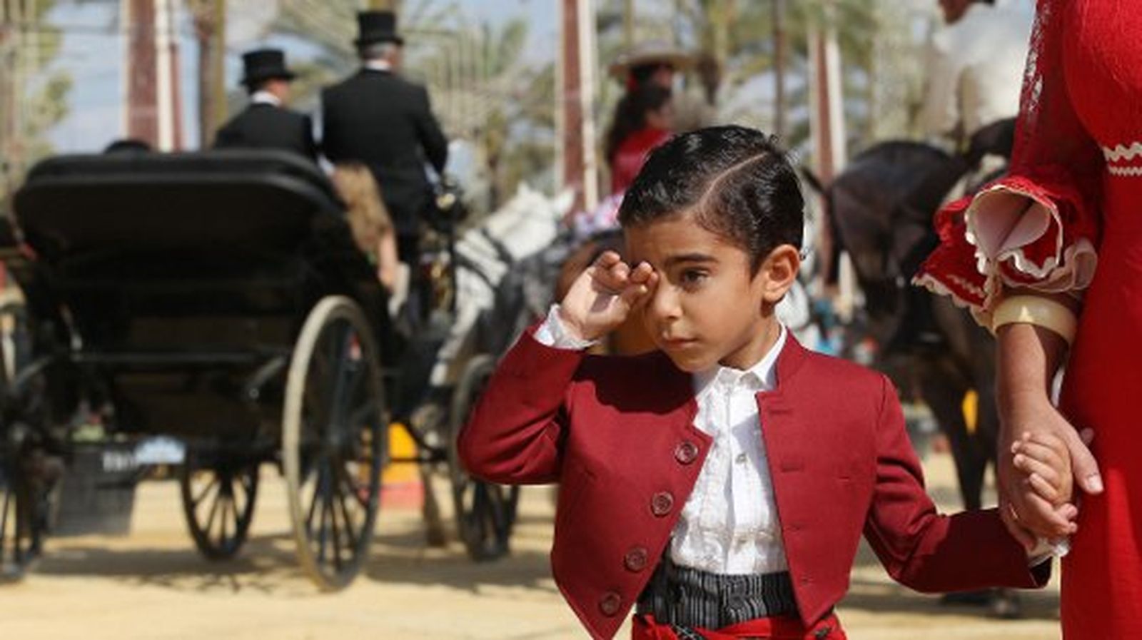 Un niño vestido de corto se frota los ojos agarrado de la mano de su madre, vestida de gitana. 

Foto: M.A. González- Pascual