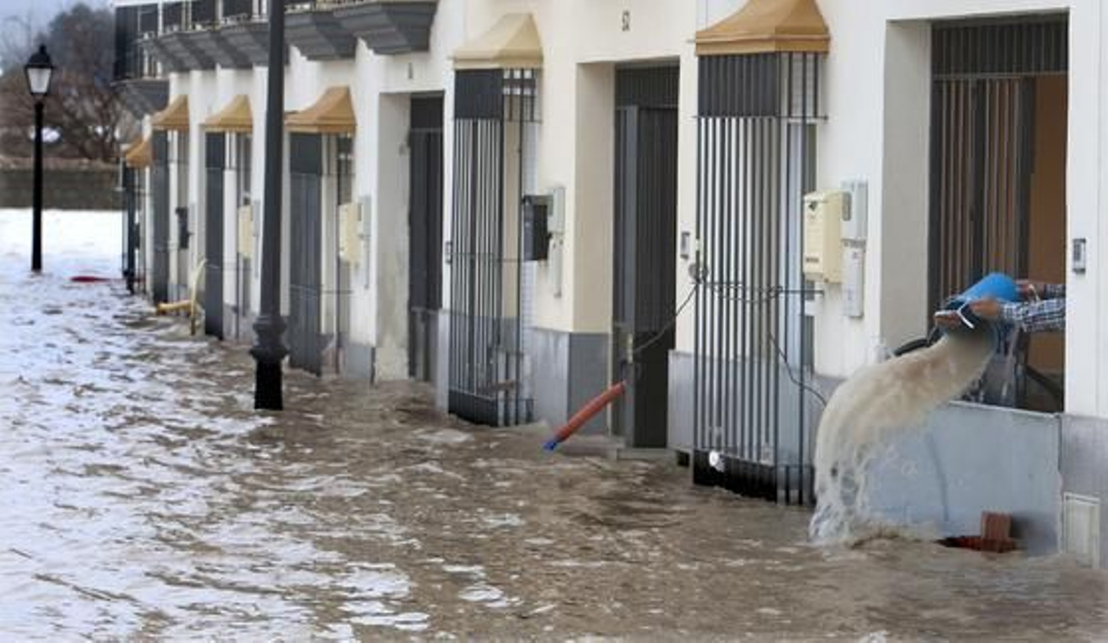 Una calle de Lora del Río inundada, y un vecino achicando agua con un cubo.

Foto: Agencias
