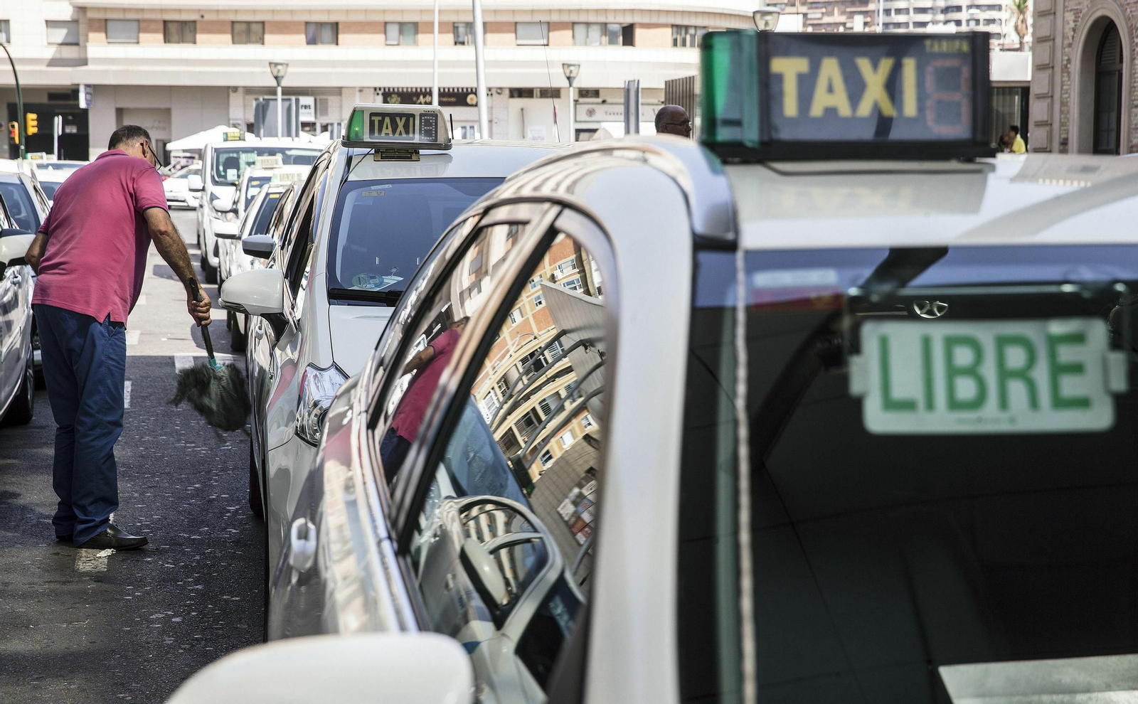 Un taxista limpia su vehículo junto a la estación de trenes Málaga María Zambrano.