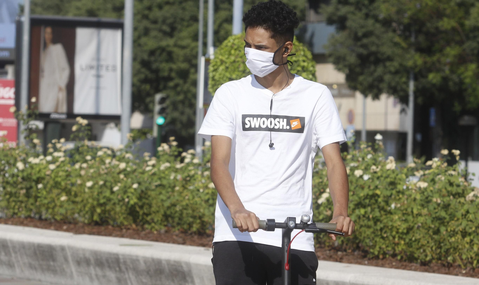 Un joven circula en patinete con mascarilla.