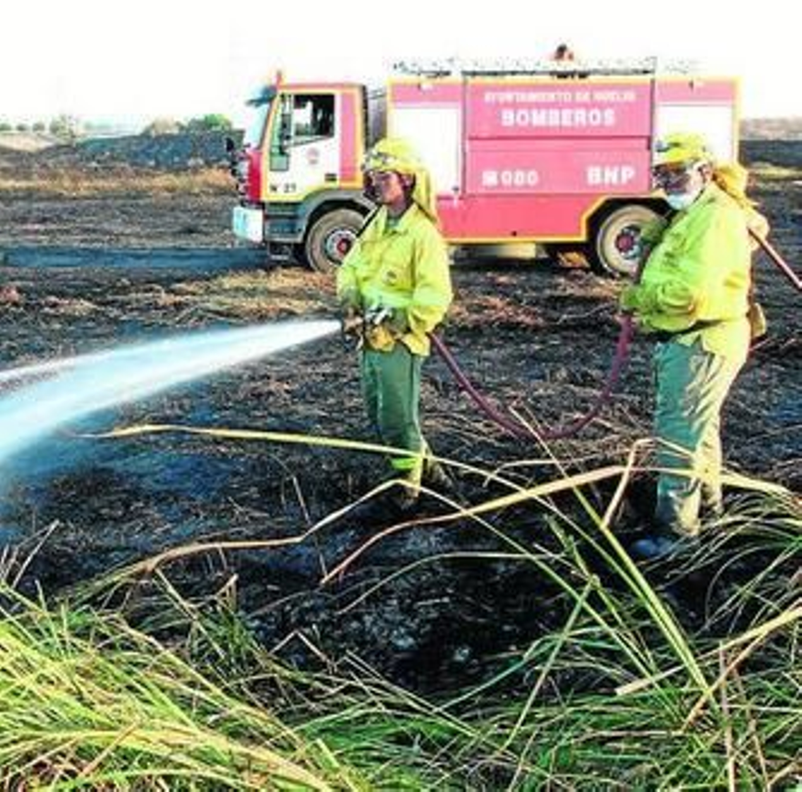 Dos operarios refrescan el terreno para evitar un rebrote del incendio.