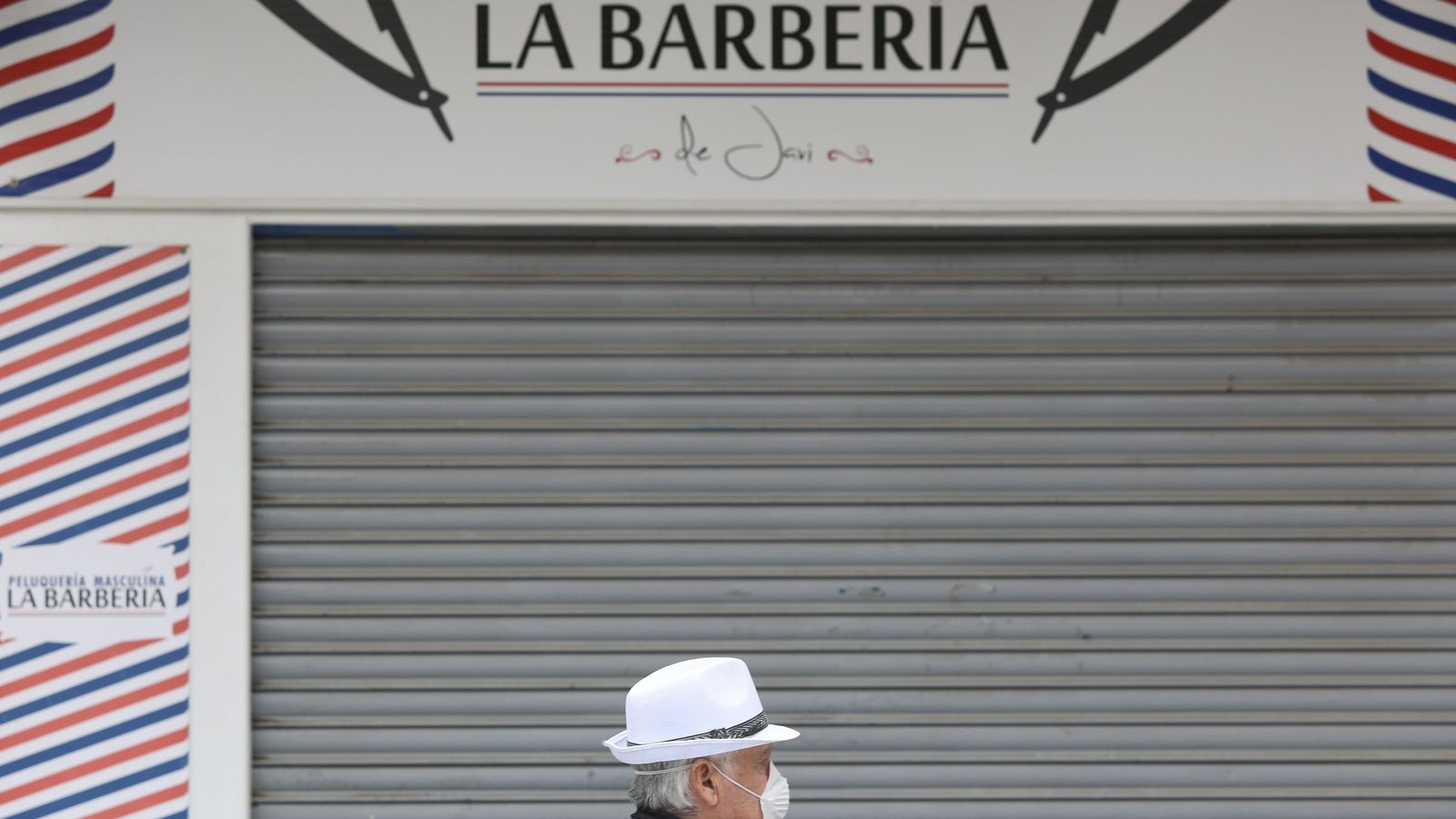 Un hombre con mascarilla pasa frente a una peluquería.
