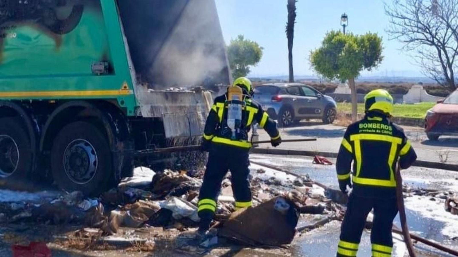 Un par de bomberos del parque de San Fernando se afana en las labores de extinción del fuego en el vehículo municipal de los servicios de limpieza