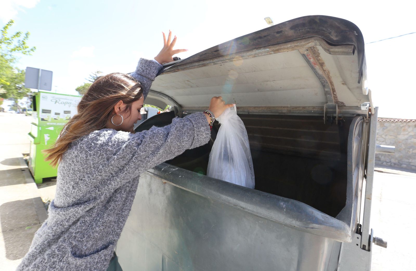 Una joven deposita una bolsa de basura en un contenedor.