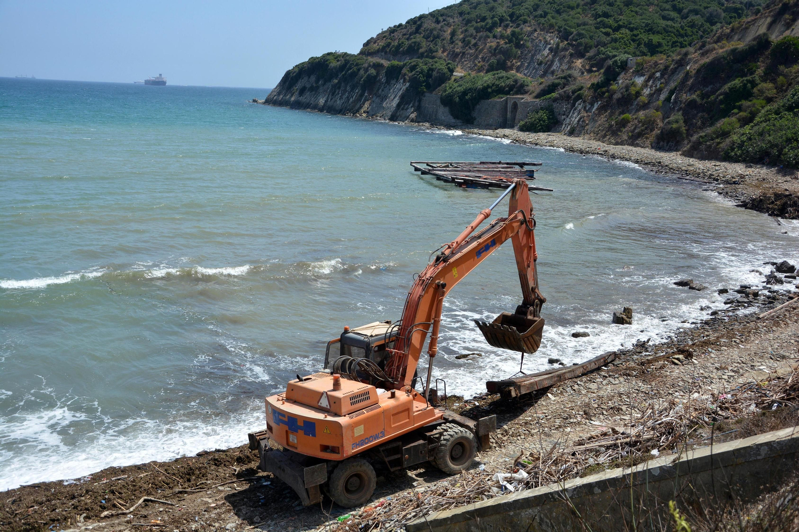 Una máquina, en plena orilla de la cala entre la madera desguazada y una batea al fondo, ayer.