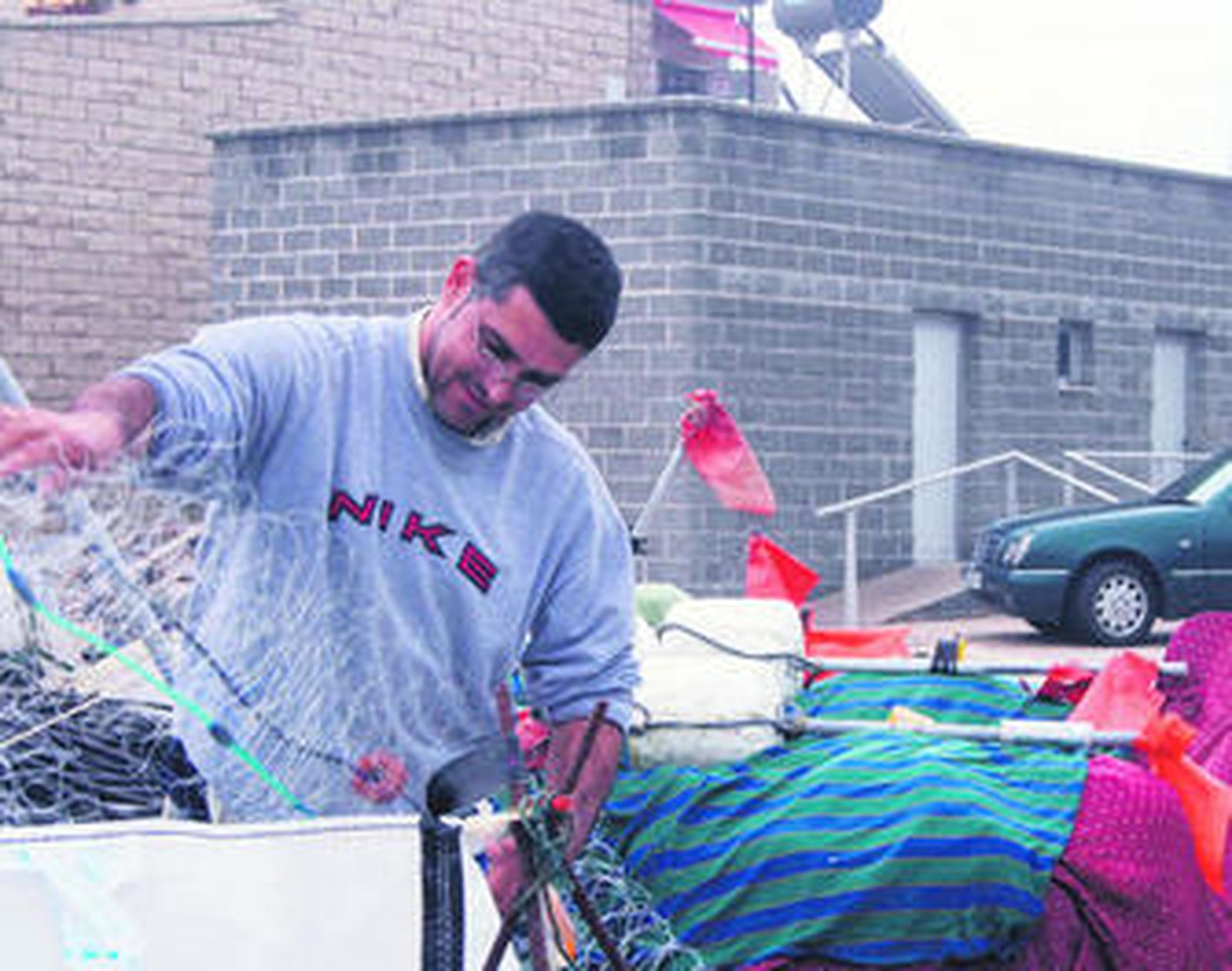 Un marinero repasa sus redes delante del módulo de aseos cerrado.