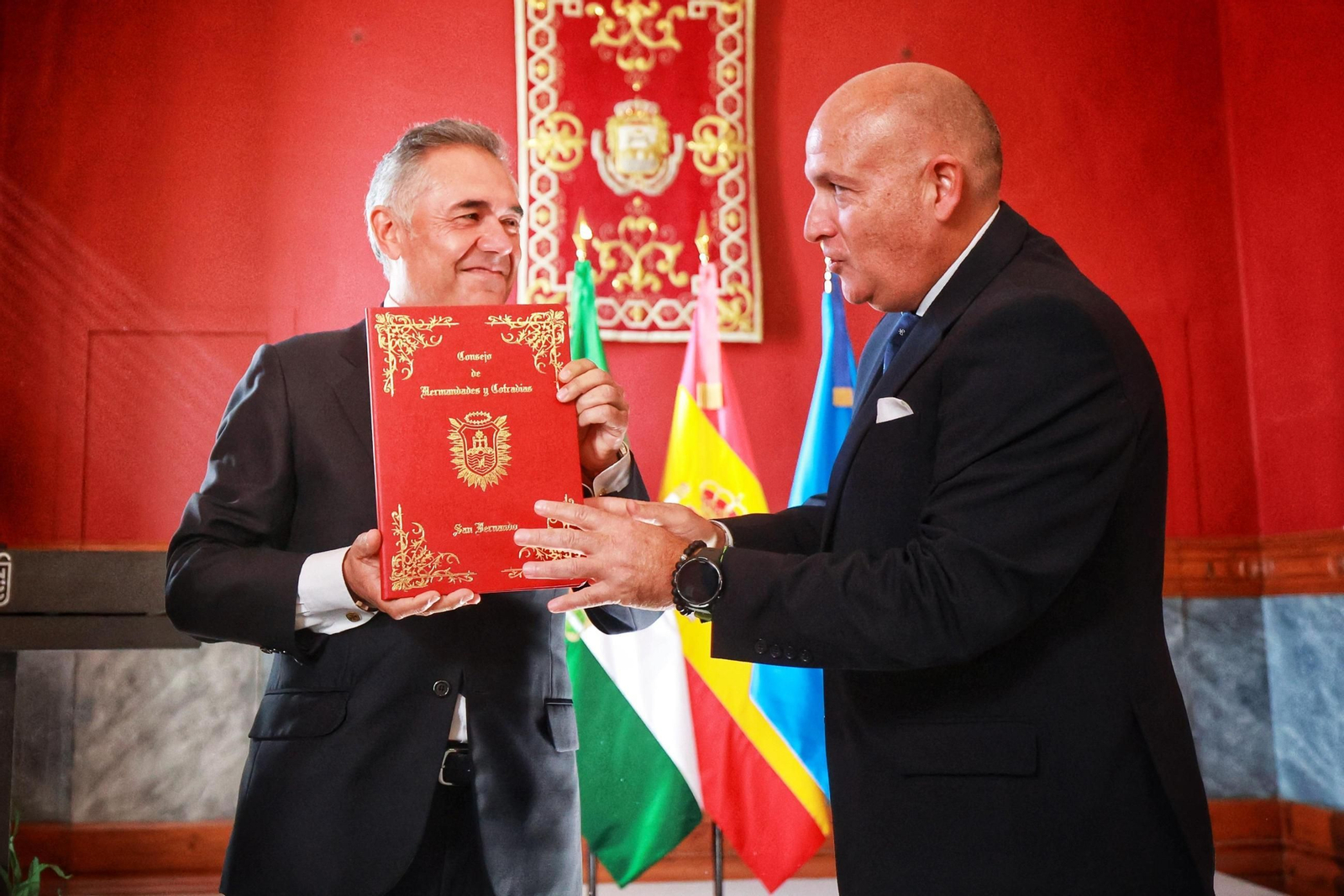 Momento en el que Eduardo Martínez, pregonero de la Semana Santa de San Fernando 2025, recibe las pastas de manos del presidente del Consejo de Hermandades y Cofradías, Manuel A. García