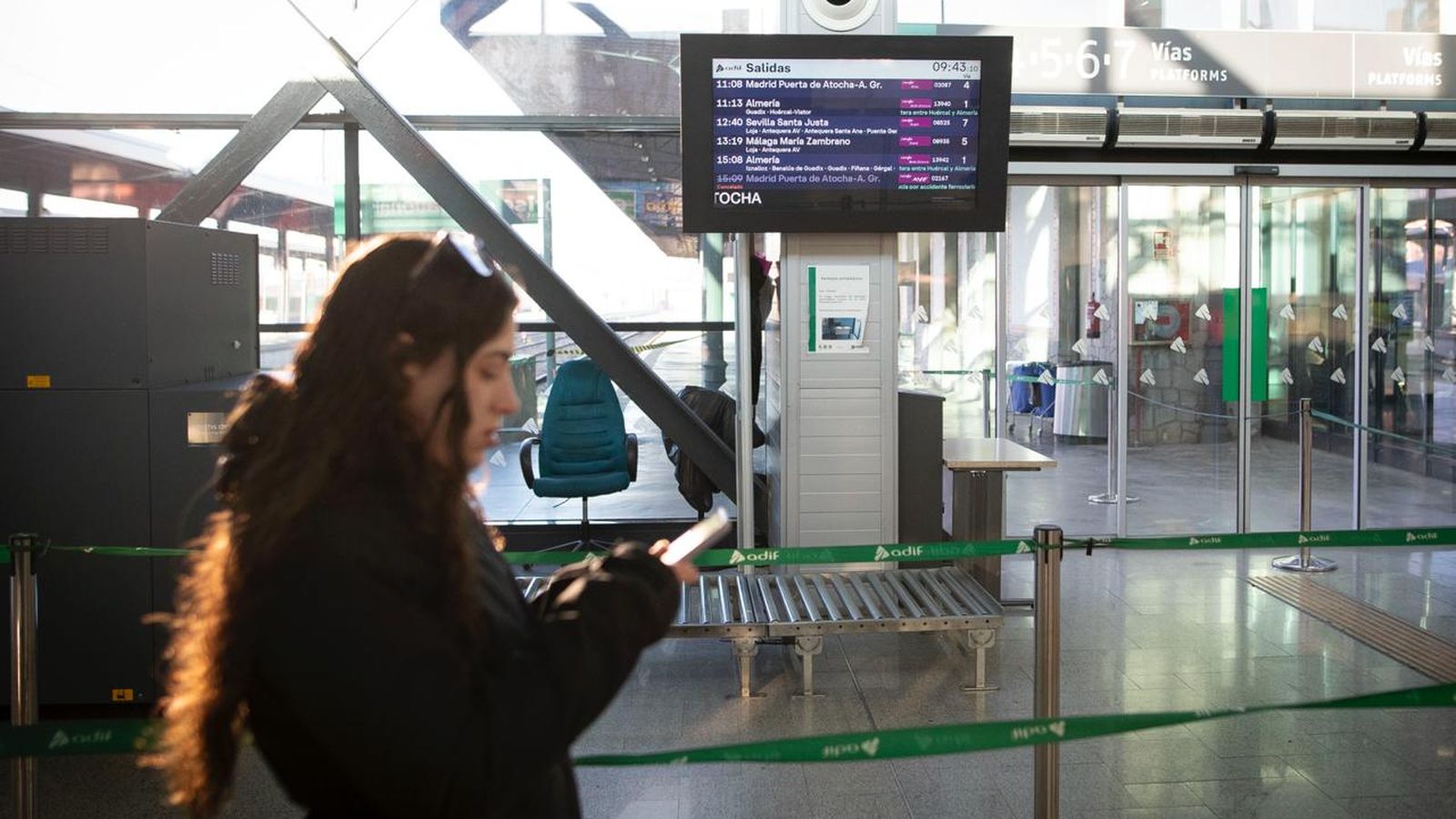 Una pasajera consulta su movil frente a las pantallas de salidas de los trenes de la estación