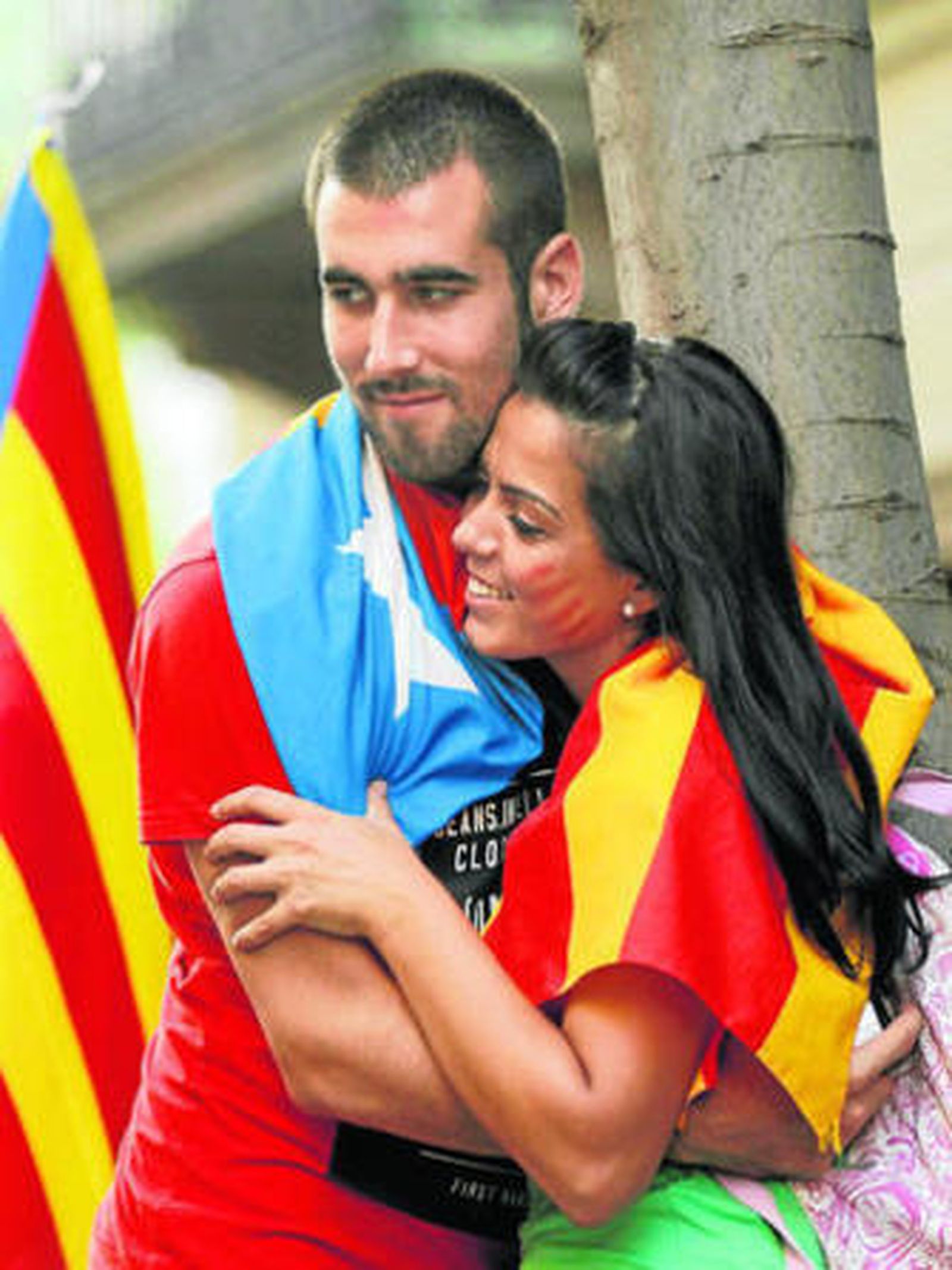 Una pareja de jóvenes independentistas se abraza con la bandera de Cataluña en sus hombros.