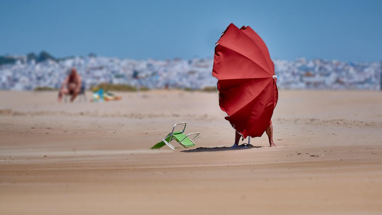 Un hombre y su sombrilla luchan contra el viento de Levante  en la playa  de El palmar.
