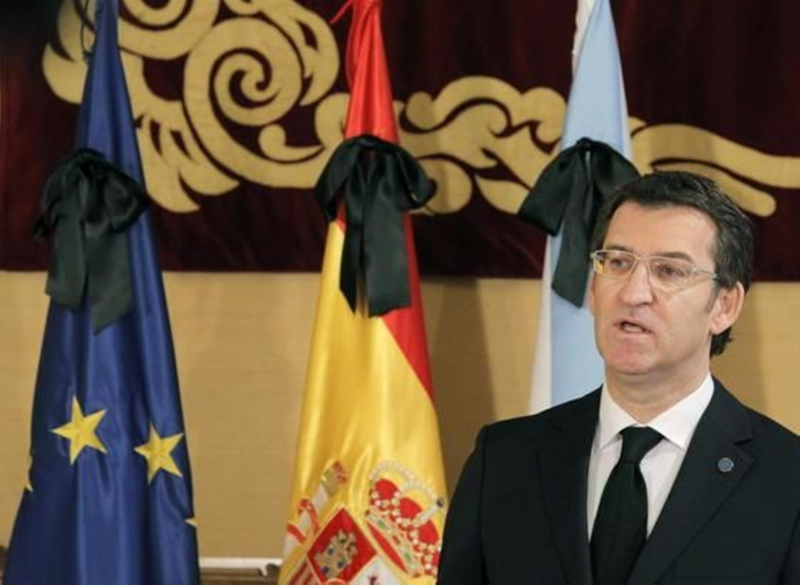 Alberto Núñez Feijoó, con las banderas europea, española y gallega ataviadas con crespones negros en señal de luto por la muerte de Manuel Fraga. / EFE