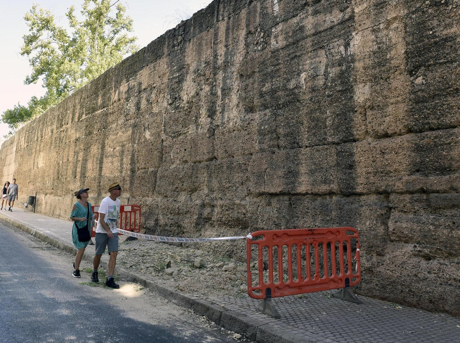 Dos viandantes observan la zona en la que ha caído una almena de la muralla de la Macarena.