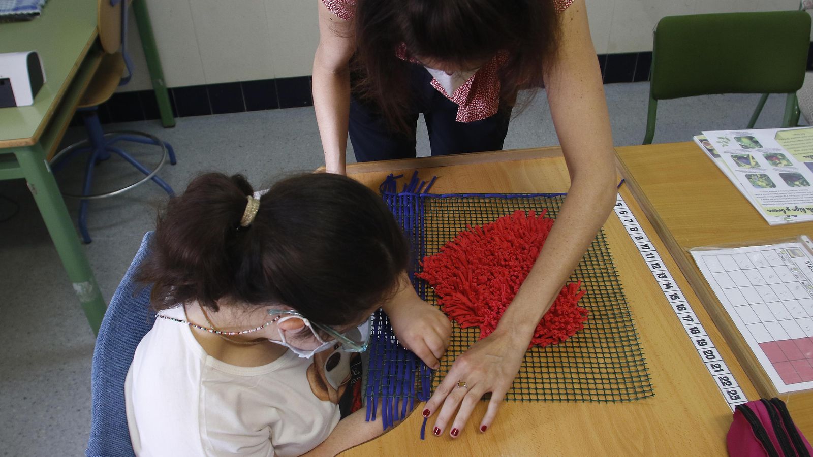 La maestra del aula específica ayuda a una estudiante a confeccionar una alfombra.