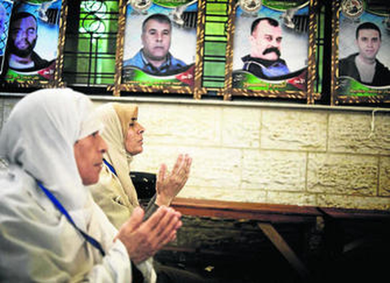 Mujeres palestinas rezan durante una protesta ante las oficinas de la Cruz Roja en Gaza, decorada con fotos de varios prisioneros.