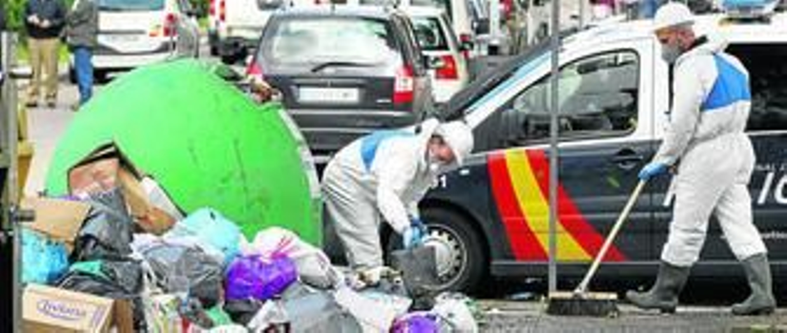 Operarios de Tragsa limpian una calle bajo protección policial, apenas unas horas después de haber sido atacados.