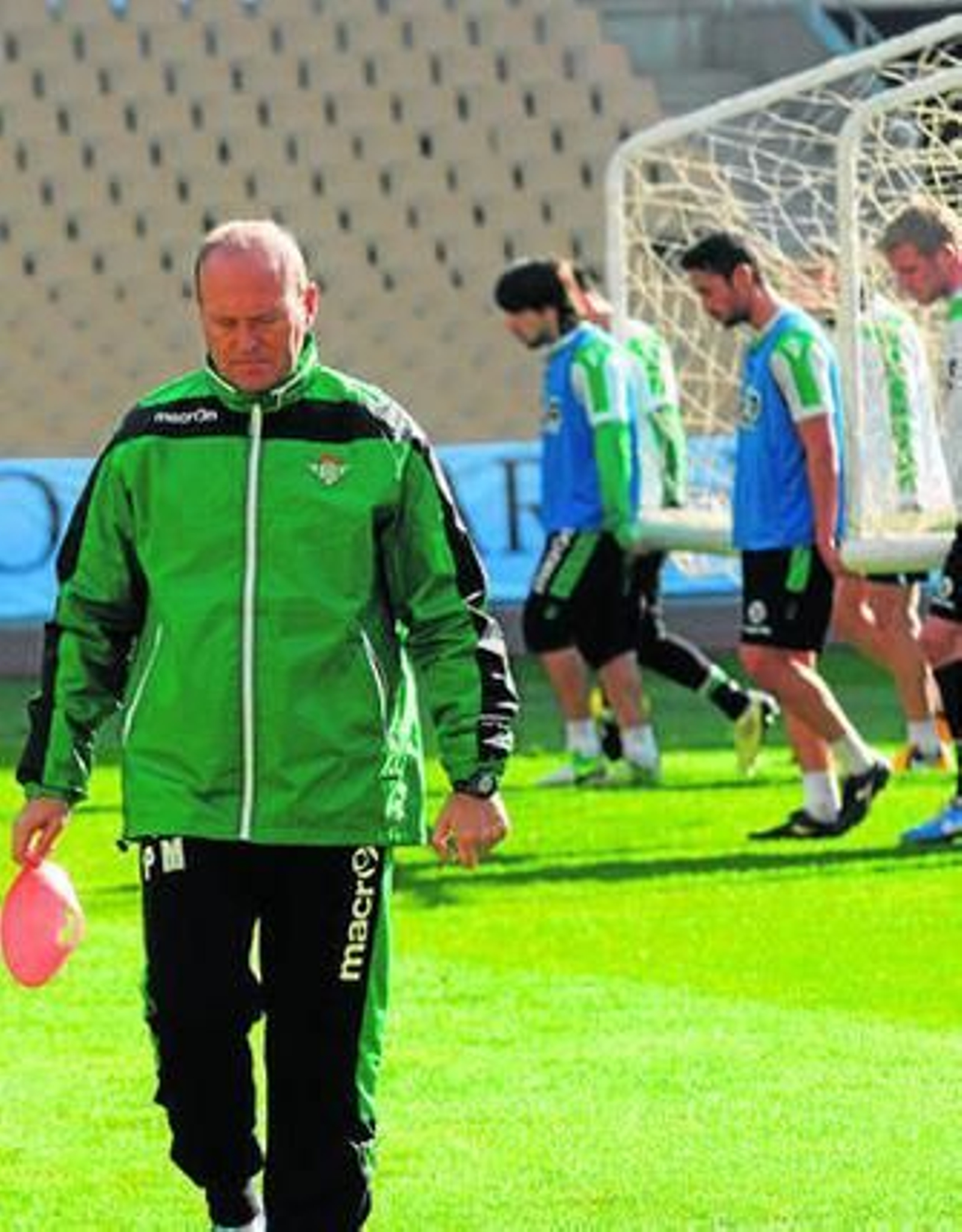 Mel camina pensativo mientras los jugadores transportan una portería.