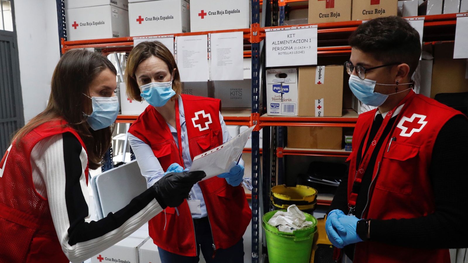 La Reina Letizia comprueba la organización del trabajo con dos voluntarios en los almacenes de Cruz Roja.