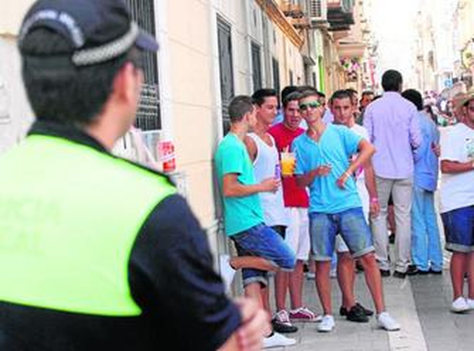 Un policía local vigila a un grupo de jóvenes haciendo 'botellón' durante la Feria en el centro.