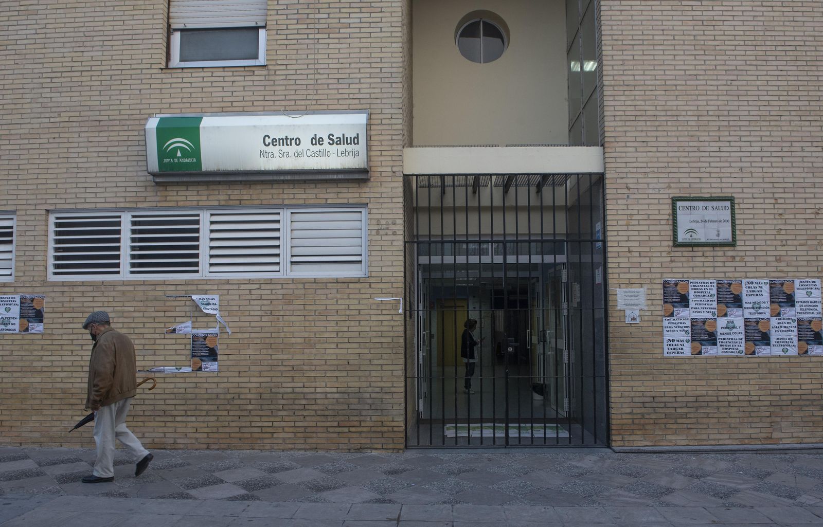 Un hombre pasa ante la puerta del centro de salud de Lebrija, donde hay colgados numerosos carteles en señal de protesta.