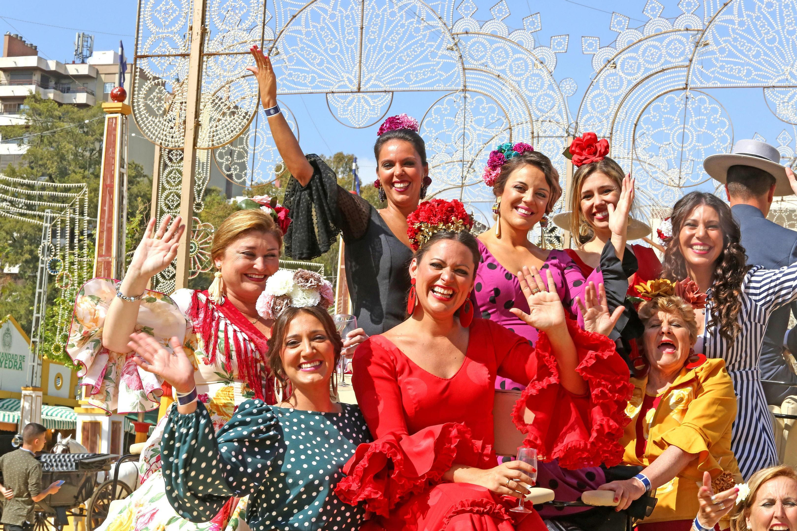 Un grupo de mujeres saluda mientras pasea por el Real en coche de caballos.
